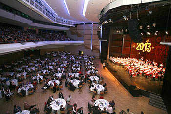 the orchestra performing on the stge, guests having dinner at round white clothed tables