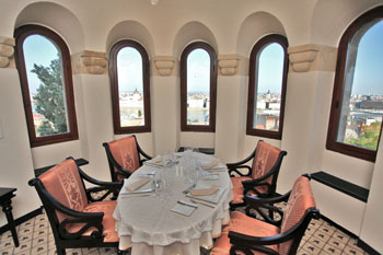 an elegantly set oval table with four pink chair, 3 vaulted windows with view of Pest