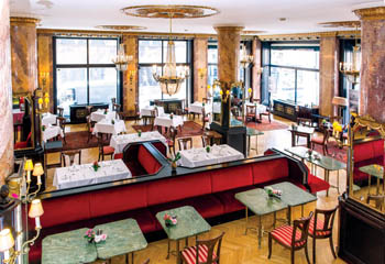 a black-topped bar with square green coffee tables, gilded chandelier huge panorama windows inside the cafe