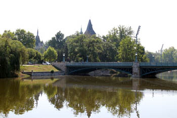 part of the greenish colored lake and a bridge, the tower of Vajdahunyad in the background