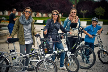 3 young ladies standing next to their e-bikes