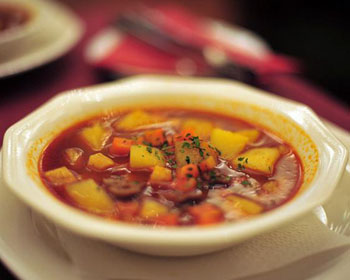 thick goulash soup with potato and carrot cubes in a white bowl