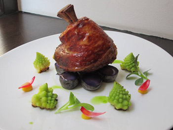 a roasted pork knuckle on pruple potato slices , with pagoda broccoli pieces around on a white round plate
