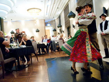 a pair in folk costume (the woman in red, green and white) dancing next to the diners