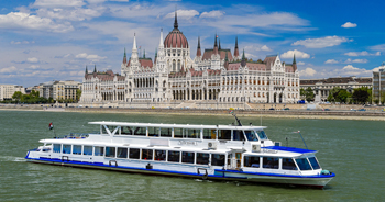 a white multi-deck ship on the Danube, the domed Royal Palace and the buildings of the Varkert in Buda in the background
