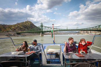 2 young couples sitting at the back of the cruise boat's upper deck (green Liberty bridge in the background)