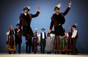 2 folk costumed men jumping in the air with 4 pairs of dancers in the background