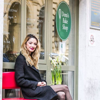 the young owner of Domi's bake shop sitting on a bench in front of the shop