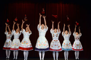 7 women folk dancers dressed in traditional costume, each holding a botter above her head 