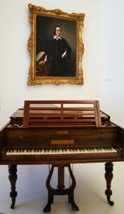an old cherry wood piano with Franz Liszt's painting onthe wall behind it