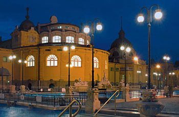 bathers enjoying the open air pools at the blue hour, the lights on inside the yeloow bath building