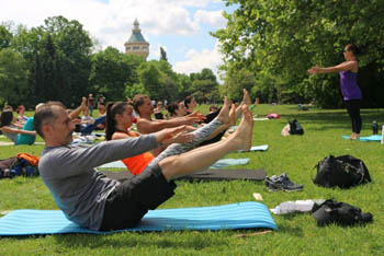 around 20 people doing yoga in the park, the tip of the water tower in the background
