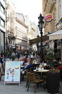 a cafe terrace with many people, a lamp post and a Burger King logo on Vaci Str.