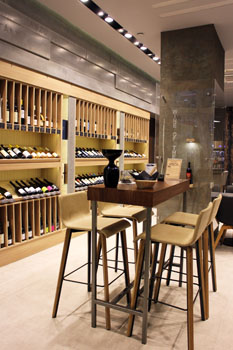 4 bar stools around a table, bottles of wine on blonde wood shelves in the background