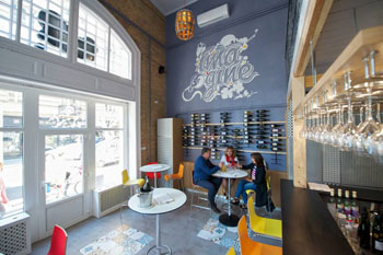 3 people sitting around a round white table, bottles stacked on shelves in the background