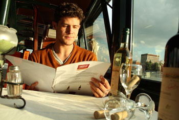 a young man reading sitting at a table anda wine list in a bar