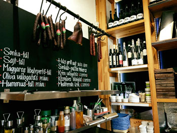the bar area with a balck board and sausages hanging, wine bottles on shelves