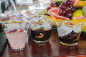 1 strawberry and 2 choco mousse with whipped cream in shot glass, fruits in the background
