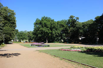 a wide walkway, flower beds and green lwan with trees on the island