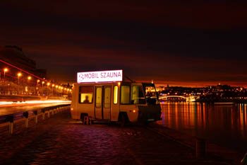 a wooden sauna cabine written Moile Sauna on its top, at night on the Danube bank