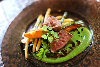 steak slices with asparagus and green pea sauce on a round copper plate