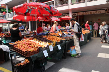 vendors selling fresh fruits and vegetables under red umbrellas on a summer day