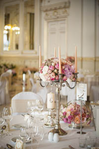 stylishly set white tables with pink flower arrangements and candles in the middle, white clothed chairs around the tables