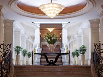 the main lobby with a grand staircase and a huge inverted pyramid shape chandelier hanging form the ceiling, white stuccoed columns along the two sides
