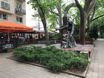 the bronze statue of Franz Liszt sitting, on the square named after him, terraced cafes in the background