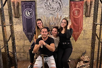 photo of a young man and 3 ladies sitting on a huge iron throne in a medieval room - at the end of an escape room game in Mystique Room