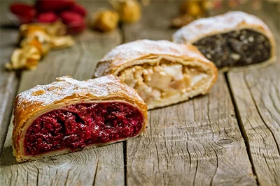3 slices of strudel placed on a wooden table: from righ to left: with sour cherry, cottage cheese, poppy seed filling