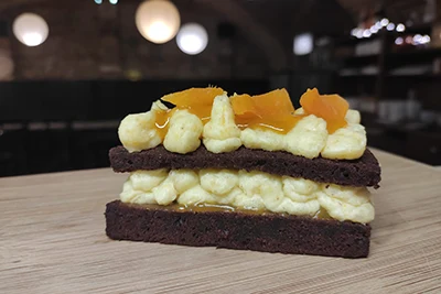 a slice of vegan cake: 2 thin layers of chocolate sponge cake filled with millet cheese cream and peach preserve 