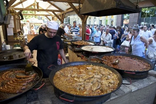 A young male chef in white cap roasting sausages in a giant pan on the outdoor Hungarian Flavours sfestival