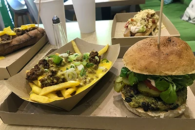 A large Juicy Lucy burger, Fries with vegan chili and cheddar sauce, and Mexican dog on cardboard plates in Vegan Love