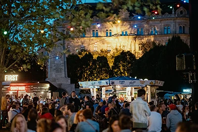 lots of people having good time at the festival at dusk, string of fairy lights above them