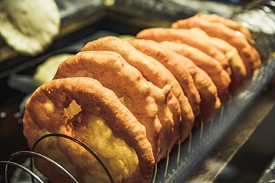 a row of lángos (round, deep fried pastry) placed on a wire rack