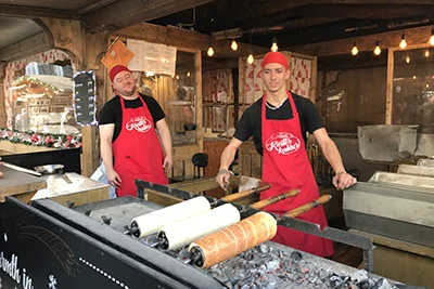 A young guy wearing a black T-shirt, a red apron and red cap baking funnel over charcoal