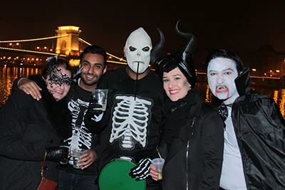 2 young ladies and 3 men dressed in Halloween costume on a photo with the illuminated Chain Bridge in the background