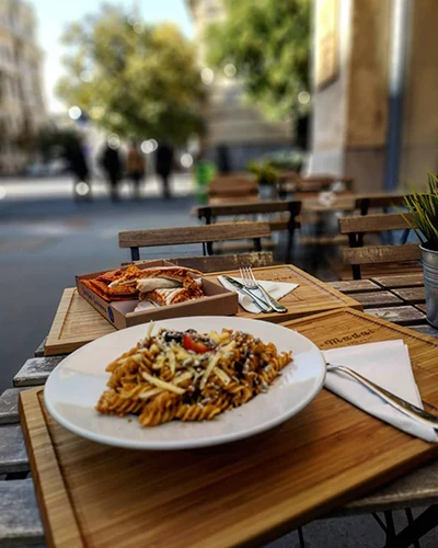 Fusilli pasta with vegan Bolognese sauce in a white bowl, plced on a small wooden table on the terrave of Madal Food Bar