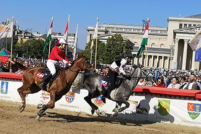 2 horse racers competing, part of the Museum Of Fine Arts in the background