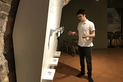 a young man wearing glasses, a white polo shirt and black trousers showing an interactive item in the museum