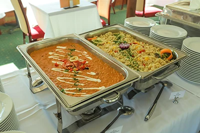 Chicken paprikash and dumplings in large, heated stainless steel food containers placed on a buffet table