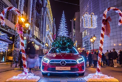 a silver Xmas tree intsallaion in front of the Kempinski Hotel and a red Merceds car with Christmas green decoration on its top