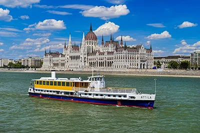a large white, blue and yellow cruise boat on the Danube with the Parliament in the background on a clear day