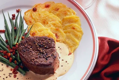 sirloin steak with French potato gratin and mushroom sauce on a round white plate