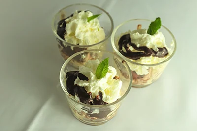 Somloi galushka - layered dessert with whipped cream on top in 3 shot glasses