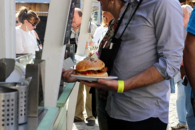 A man in a pale blue shirt holding a burger on a white plate in his left hand