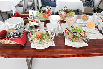 salads and various spreads in glass serving bowls on a cherry wooden buffet table