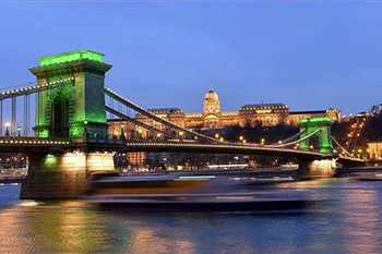The Chain Bridge illuminated in green in the evening. The Royal Palace in Buda lighted up for the night can be seen in the background.