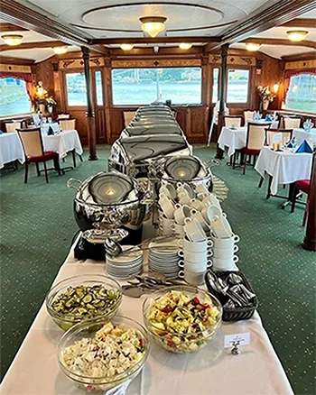 A long buffet table on a panorama cruise ship. Stainless steel food containers, plates, bowls, spoons and other utensils placed on it.